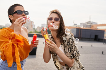 Friends celebrate joyfully on a rooftop with bubble wands during a sunny afternoon party