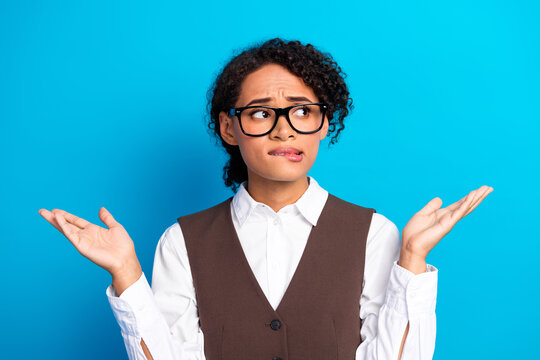 Young female student in formalwear with glasses shrugged against blue background