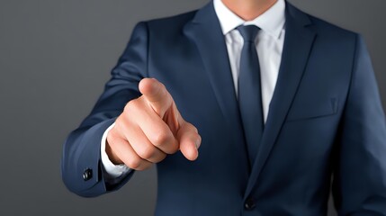 Businessman in navy blue suit pointing finger forward against gray background, conveying leadership and decision-making in professional setting.