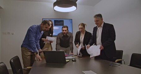 Businesspeople discuss financial documents and laptop in office meeting. Teamwork and collaboration lead to success. Business meeting, office work, and documents. - Powered by Adobe
