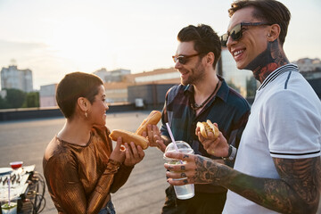 Young friends celebrate joyfully on a rooftop with snacks and drinks during sunset
