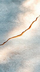 A close-up view of a cracked concrete surface bathed in warm golden light, casting soft shadows. The crack is prominent and filled with a darker, textured mater