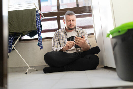 Man relaxing on balcony using smartphone next to laundry - Powered by Adobe