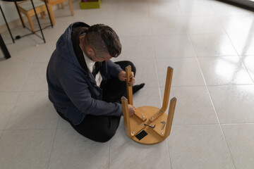 Man assembling wooden stool furniture on floor