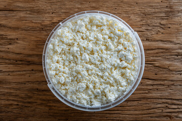 White cottage cheese or fresh milk curd in a plastic container, closeup, top view. Homemade cottage cheese texture