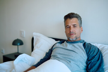 Fototapeta premium Man lying in bed wearing pajamas, feeling unwell and tired, having trouble sleeping. Concepts of insomnia, rest, exhaustion