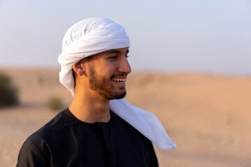 Close up portrait of happy man wearing traditional arab clothing, standing in hot arabian desert. High quality photo