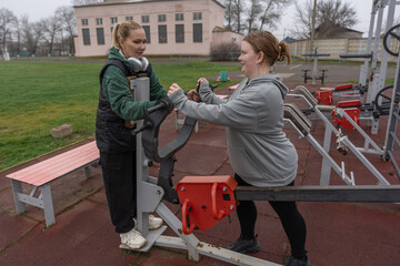 Outdoor fitness training with two women on public exercise equipment