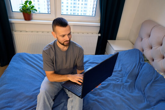 A man types on his laptop while lying on the bed in his bedroom. He enjoys remote work as he connects to online tasks from home during a moment of rest - Powered by Adobe