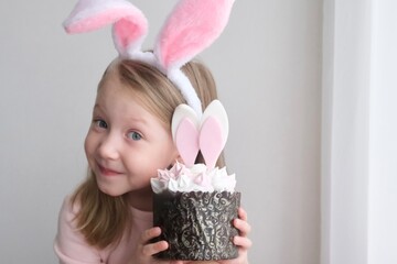 A little girl holds a creative Easter cake with bunny ears, a concept for a happy Easter holiday
