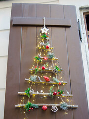 Creative handmade Christmas tree made from wooden branches, pine cones, and festive red ornaments is beautifully decorated with warm fairy lights and hung on a rustic wooden door.