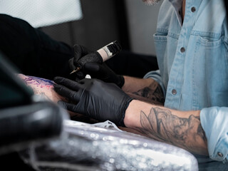 Fototapeta premium Artist working on colorful landscape arm tattoo during studio session