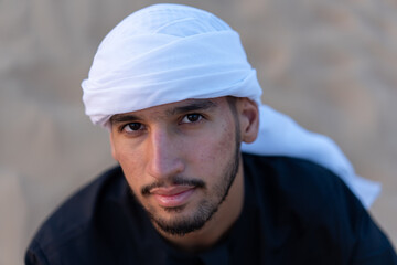 Arab man sitting on sand in the desert during golden hour, wearing traditional arab clothing. High quality photo