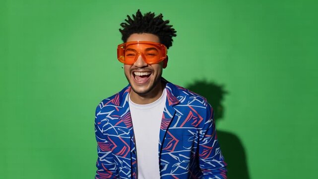 Smiling man wearing bright patterned jacket and orange goggles against vibrant green background
