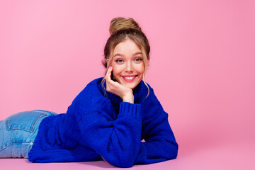 young woman in blue knit sweater lying on pink backdrop smiling at camera