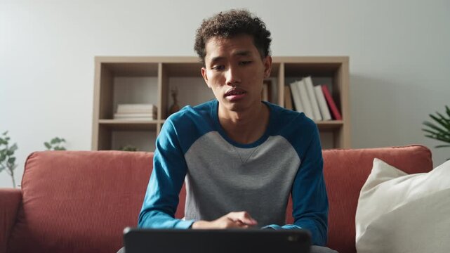 Asian teenage man learning sign language via internet with technology on tablet at home