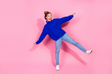 Young woman in blue sweater and jeans jumping with joy on pink studio background for fashion...