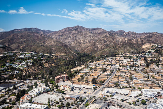 Aerial view of suburban neighborhoods beside wildfire-damaged lots in Southern California, contrasting green residential areas with scorched brown terrain