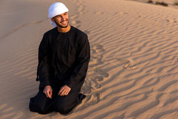 Arab man sitting on sand in the desert during golden hour, wearing traditional arab clothing. High quality photo