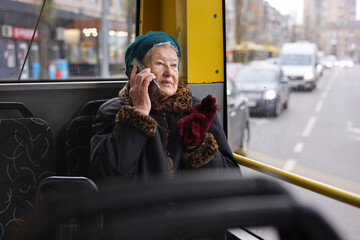 A senior woman is sitting on a bus, using her smartphone. She is traveling through the city, enjoying her journey in a relaxed manner.