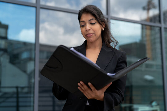 Business professional reviewing documents outside a modern office building in a city setting - Powered by Adobe