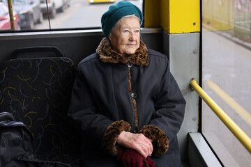 A senior woman is sitting on a bus, using her smartphone. She is traveling through the city, enjoying her journey in a relaxed manner.
