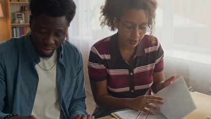 Concerned couple sitting at home reviewing overdue bills and managing finances together, calculating expenses and planning household budget - Powered by Adobe