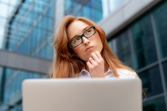 Young woman pondering at a laptop in an urban office setting during the day
