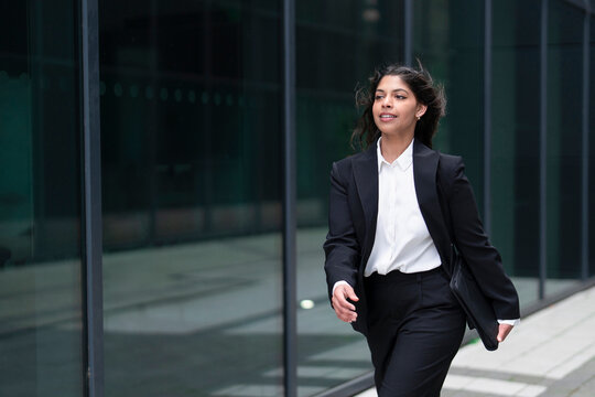 Confident business professional walking outside modern office building in urban setting during sunny day