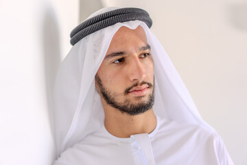 A man wearing a white robe and a black turban is looking at the camera. He has a beard and a mustache