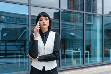 Businesswoman in formal attire talking on phone outside modern office building