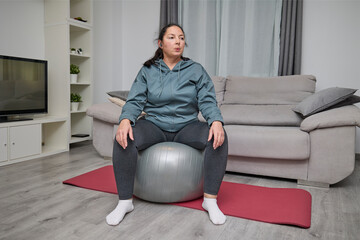 Woman sitting on a large fitness ball as part of a home exercise routine in the living room.