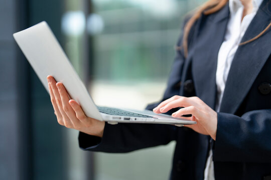Business professional using laptop while standing in modern office environment - Powered by Adobe
