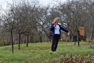 Woman walking outdoors in an orchard with a red mug