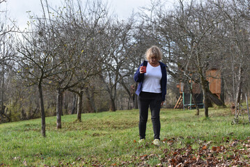 Woman walking outdoors in an orchard with a red mug