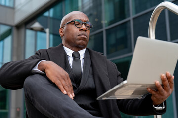 Businessman working on laptop outside modern office building in urban setting during daytime