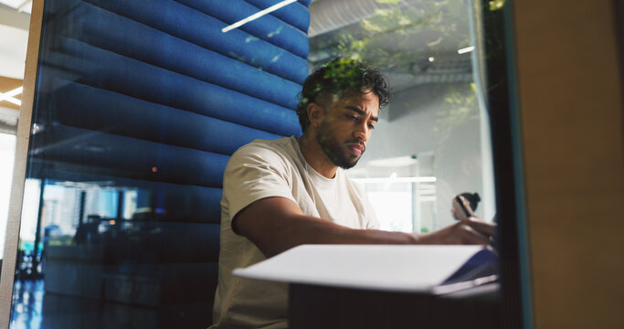 Writing, thinking and businessman in office with notebook for planning creative project in pod. Booth, professional and magazine editor working on article with research for publishing in workplace.