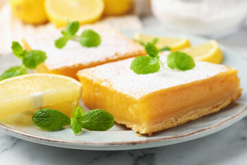 Tasty lemon bars with powdered sugar, mint and fresh fruits on white marble table, closeup