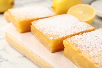 Tasty lemon bars with powdered sugar on white marble table, closeup