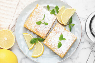 Tasty lemon bars with powdered sugar, mint and fresh fruits on white marble table, flat lay