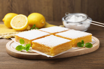 Tasty lemon bars with powdered sugar and mint on wooden table, closeup