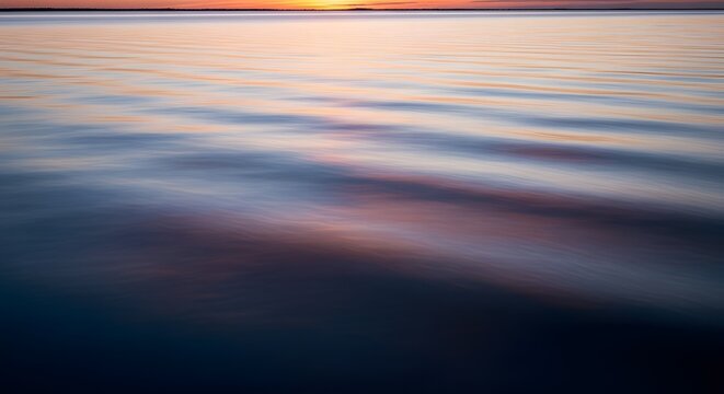 A serene view of calm water reflecting the soft hues of the sky during sunset or sunrise