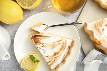 Slice of tasty lemon meringue tart with mint served on light grey table, flat lay