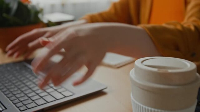 Close-up shot of unrecognizable woman in orange cardigan opening up her laptop while sitting at desk