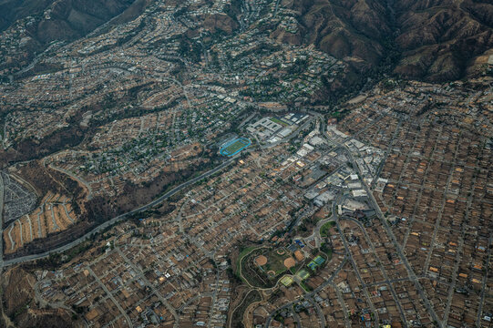 Aerial view of hillside residential neighbourhoods and sports fields in Los Angeles County, California, showing dry mountain terrain and suburban grid patterns on a clear sunny day