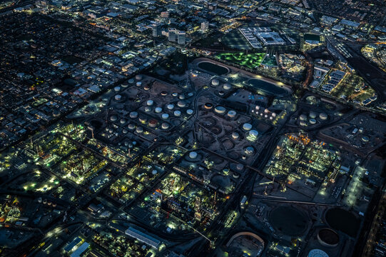 Aerial night view of industrial refinery complex and surrounding urban area in Los Angeles County, California, showing illuminated tanks, factories, and infrastructure