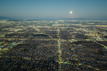 Aerial view of illuminated Los Angeles grid at night under a full moon, showing vast urban sprawl, streets, and city lights extending to the horizon across Southern California