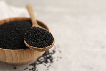 Aromatic black caraway in wooden bowl and spoon on light grey table, closeup. Space for text