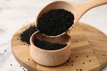 Pouring aromatic black caraway into bowl at white marble table, closeup