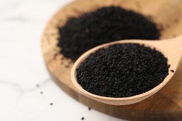 Aromatic black caraway in wooden spoon on white marble table, closeup. Space for text